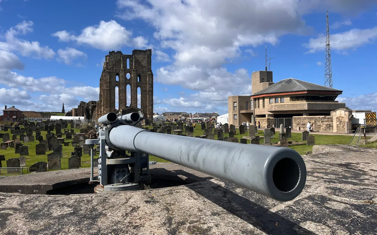 A restored gun on the Tynemouth coast battery, aimed out towards the mouth of the Tyne, with the priory's ruined east end and rose window beyond.